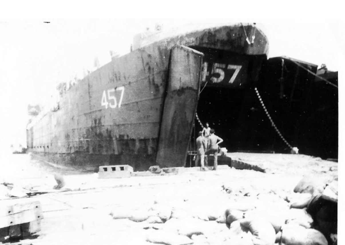 USS LST-457 — close-up of bow with hull number 457 painted on both sides, sailors at the ramp