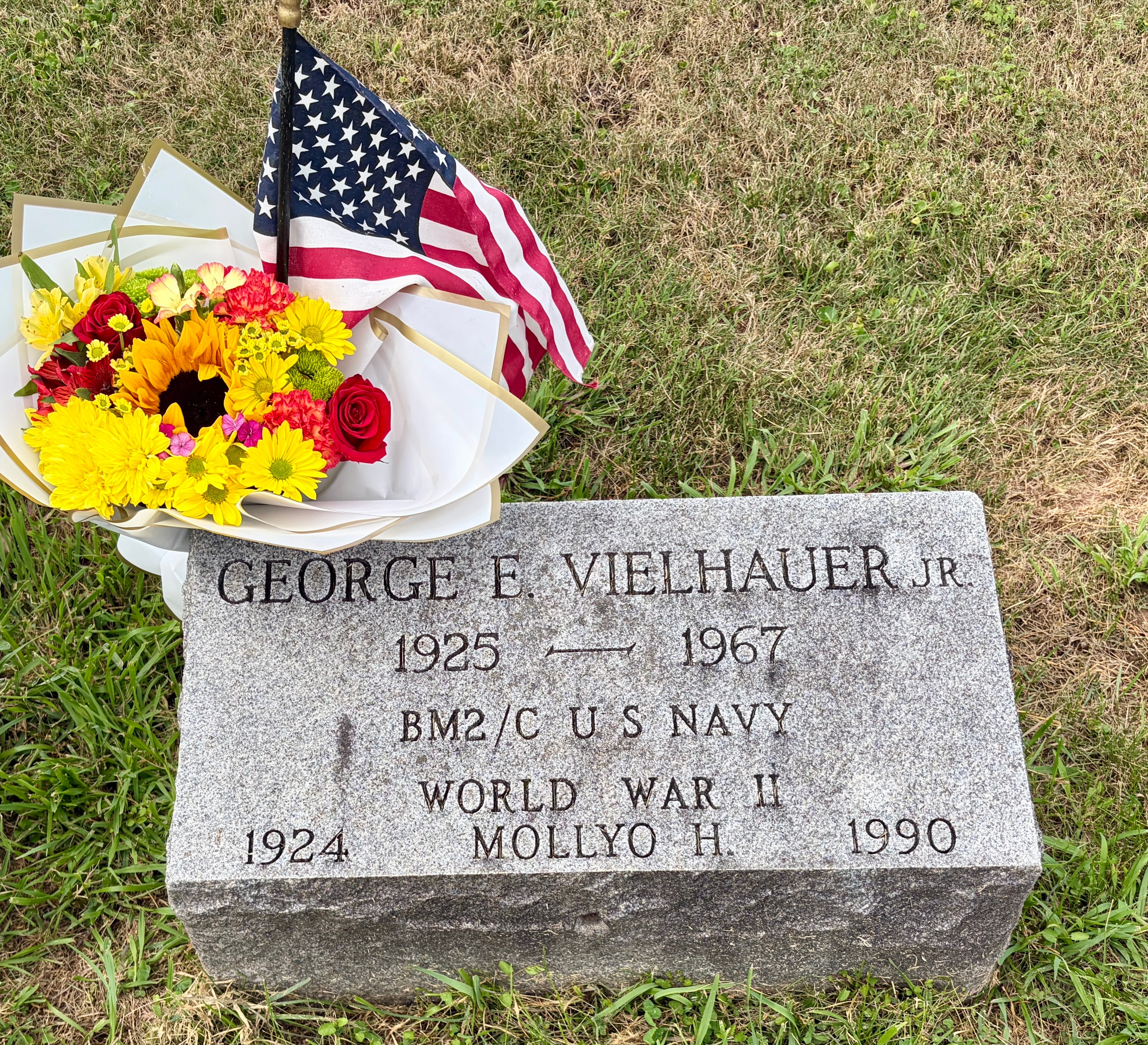 Gravestone of George E. Vielhauer Jr., 1925–1967, BM2/C U.S. Navy, World War II, with flowers and an American flag placed at the stone. Mollyo H. Vielhauer, 1924–1990, is also inscribed. Riverside Cemetery, Norristown, Pennsylvania. Photographed August 14, 2026.